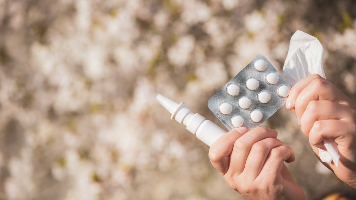 Allergy concept, young woman with pills or drugs and nose or nasal spray against the strong allergy in hand in front of blooming a tree during spring season, healthcare